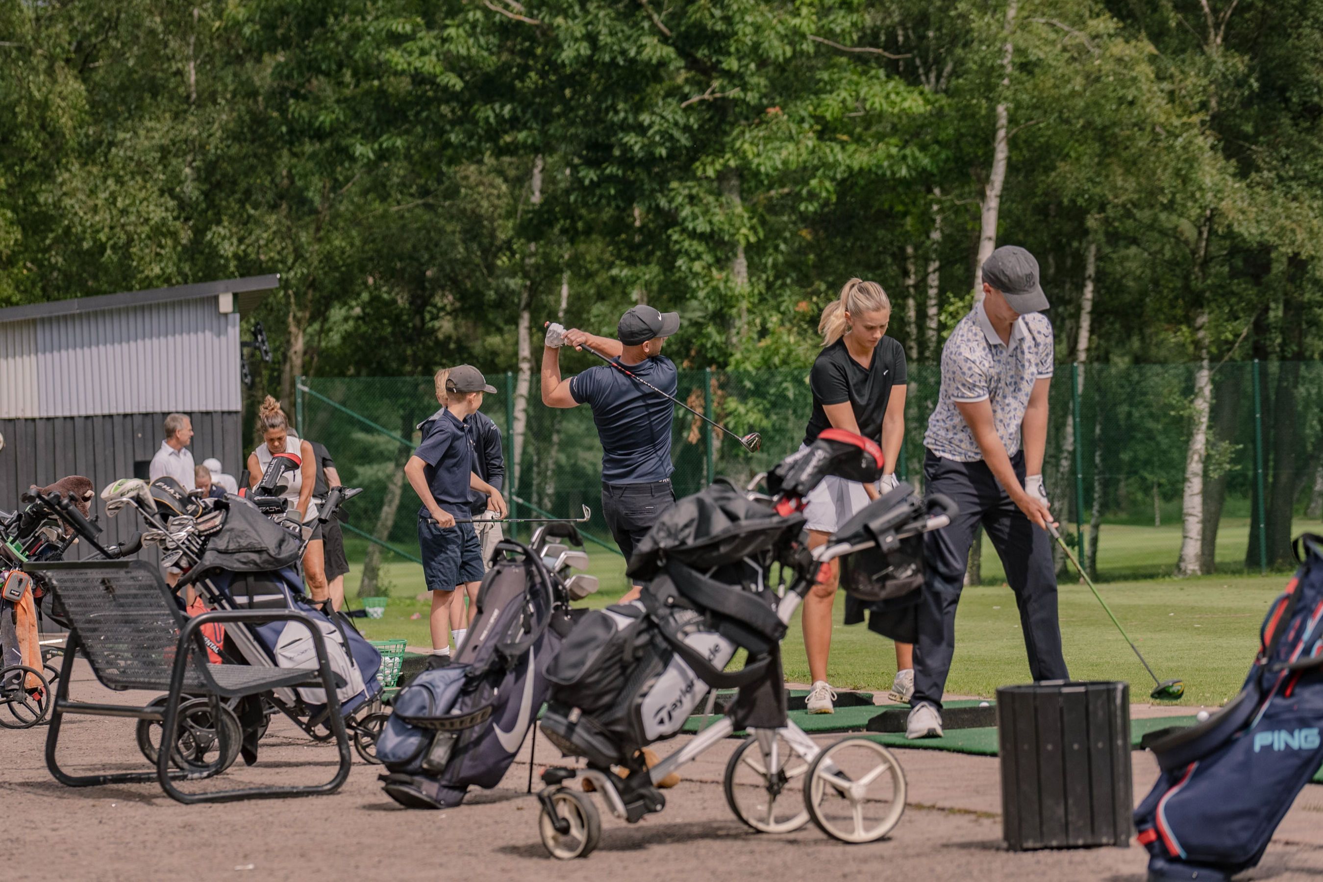 Tjejer och killar tränar golf på en range.